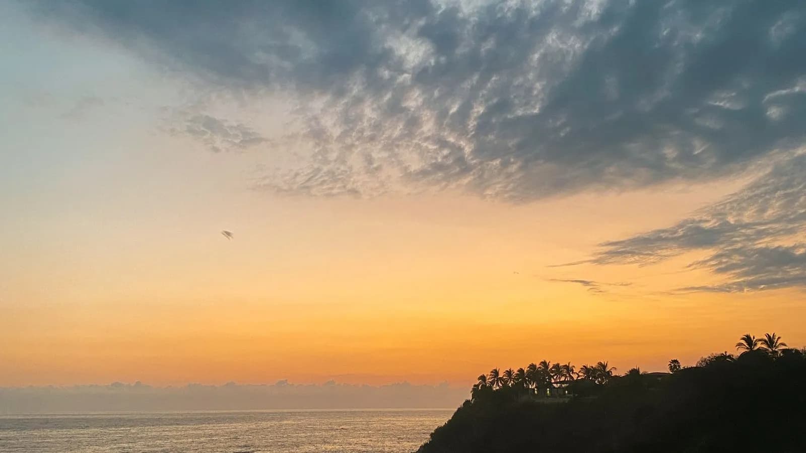 Sunset over the sea with glowing clouds seen from a hillside