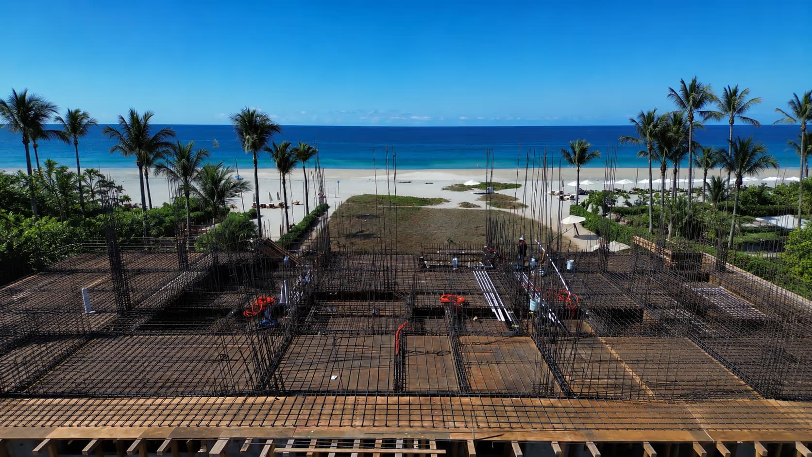 Rebar foundation of a building under construction with palm trees and the sea behind