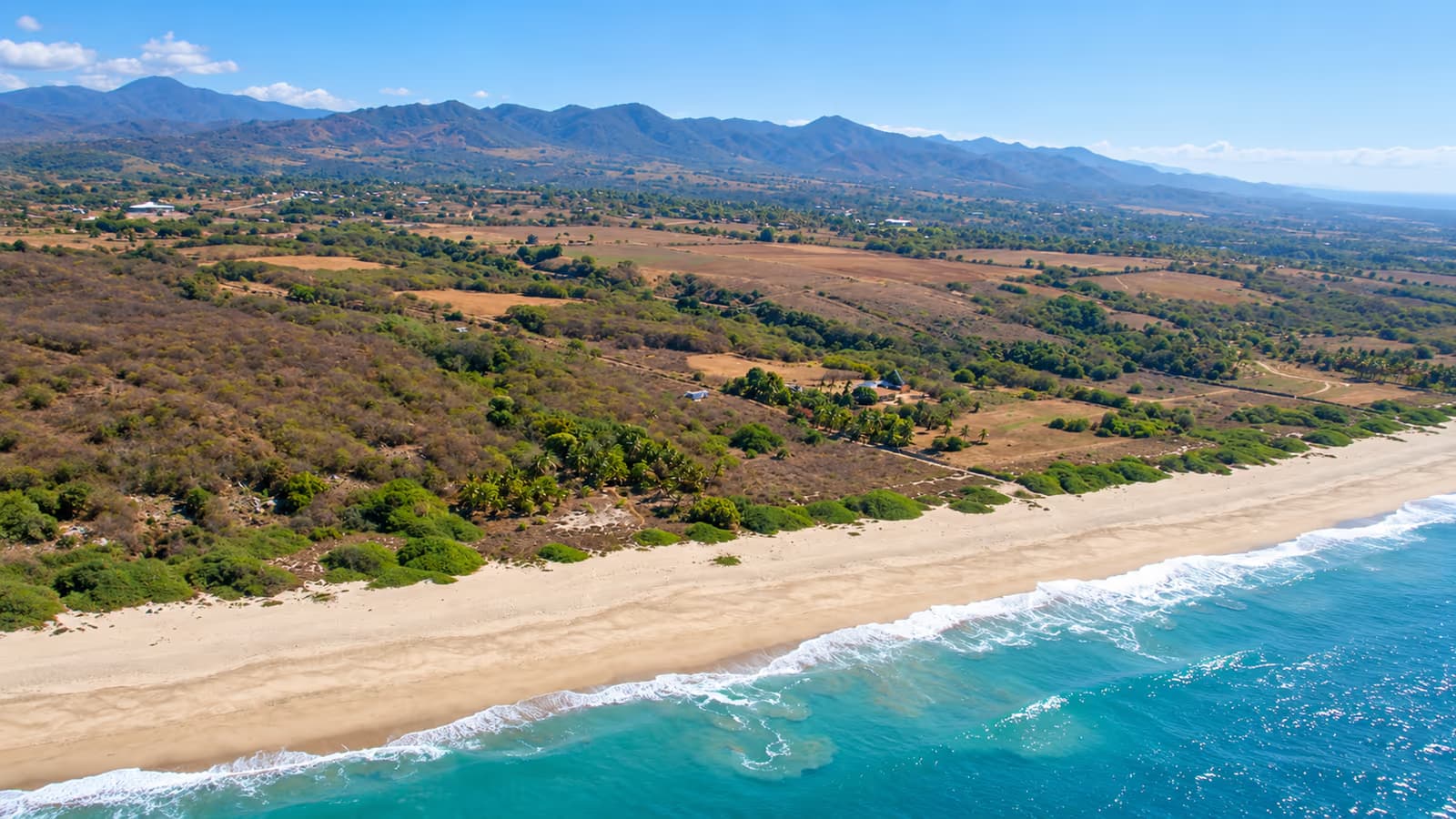 Vista aérea de una playa extensa y poco urbanizada con montañas al fondo