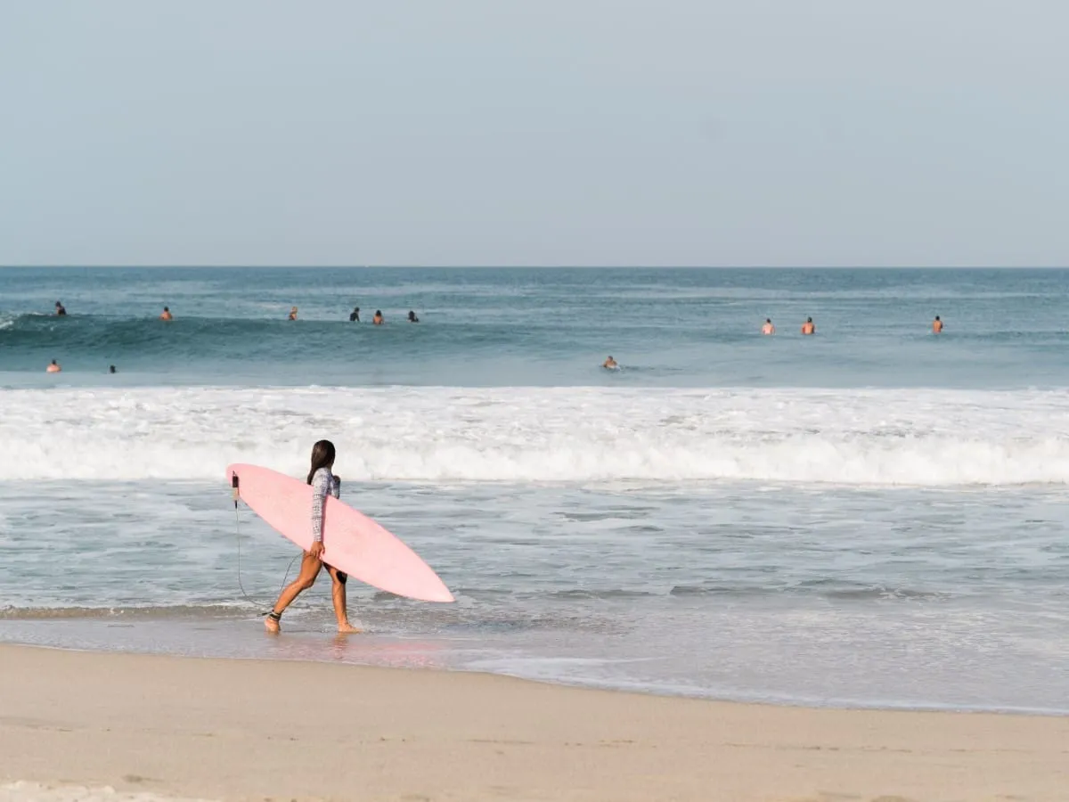 Surfer walking along the shore with a board while others wait for waves