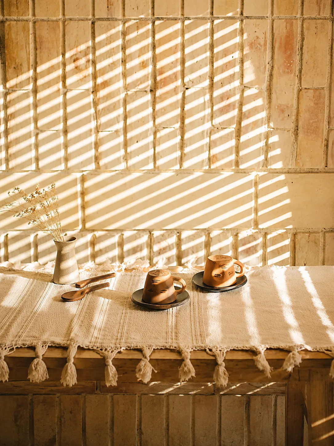 Cafe table with cups and pastries under striped light from a lattice screen