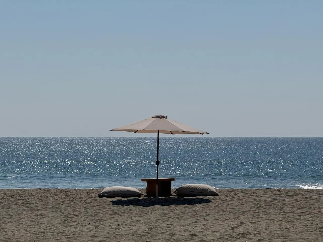 Beach umbrella and cushions on dark sand facing the sea