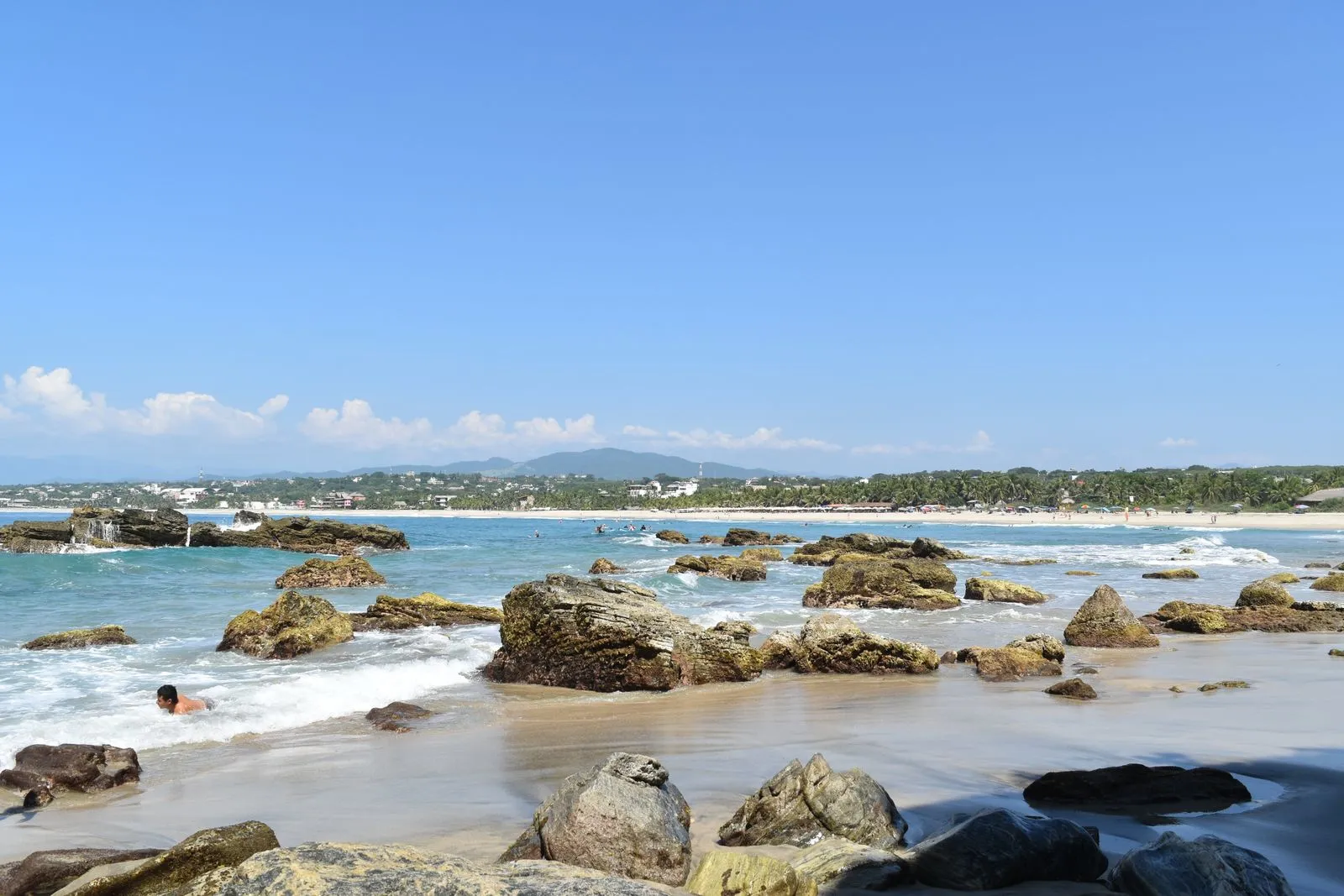 Rocky beach with surf and the town of Puerto Escondido in the background
