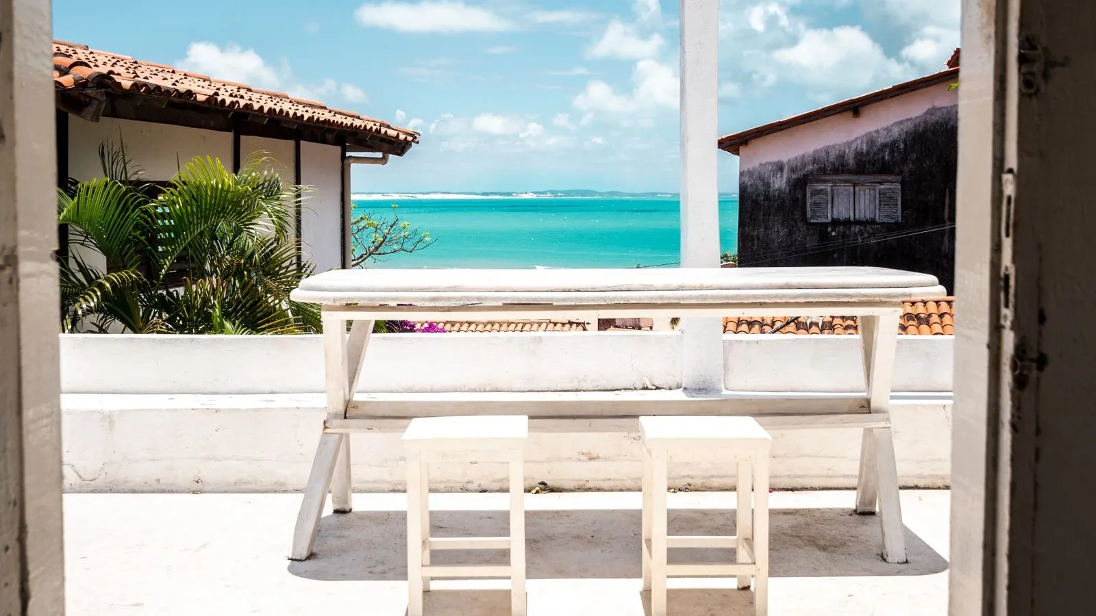 Terrace with a white table and stools facing the turquoise sea