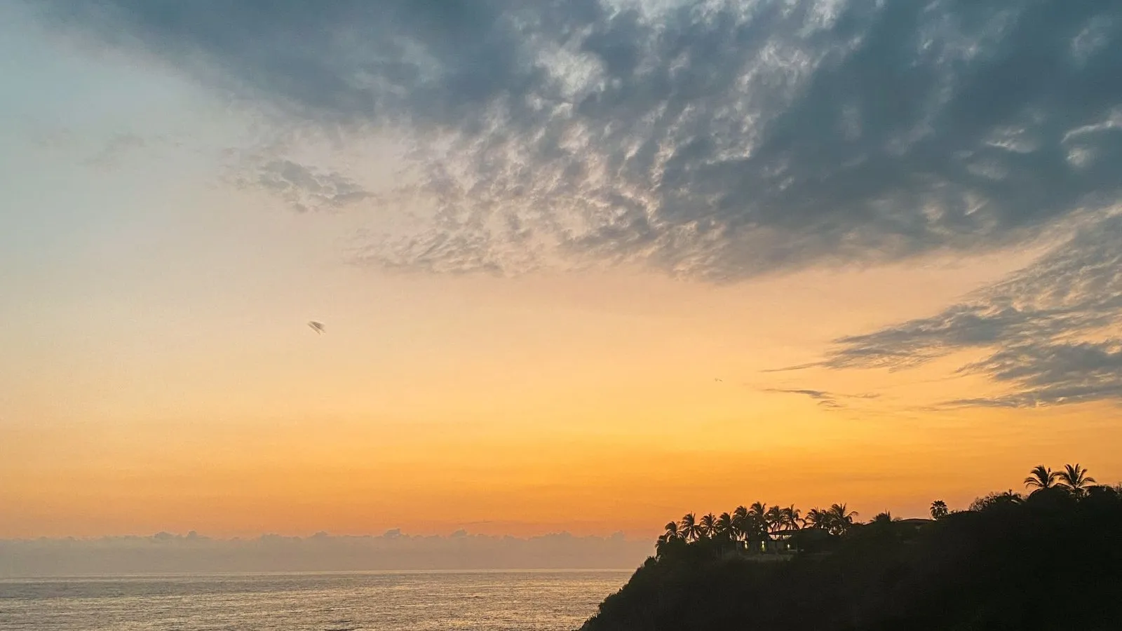 Sunset over the sea with glowing clouds seen from a hillside