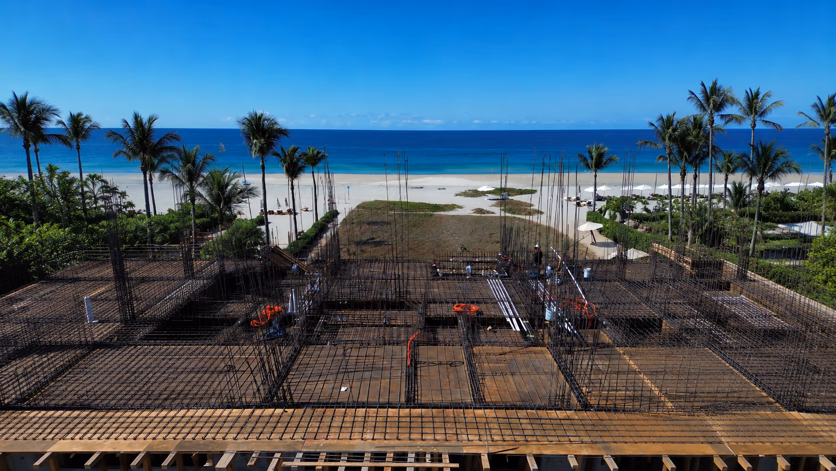 Rebar foundation of a building under construction with palm trees and the sea behind