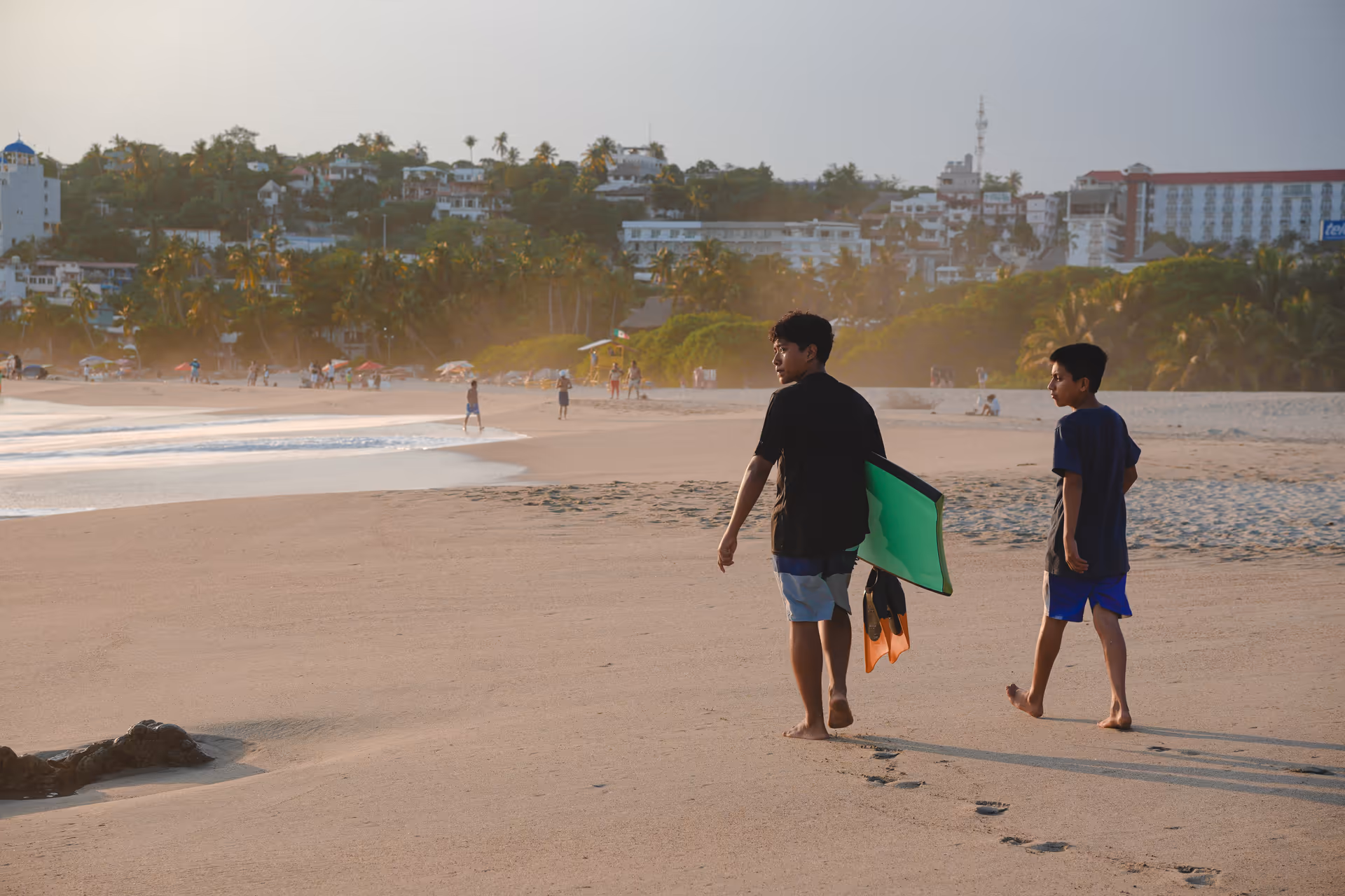 Two people walking along the shore at dusk carrying a bodyboard